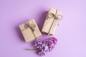 Two gifts in eco-friendly craft paper packaging on a light, lilac background with a branch of lilac.