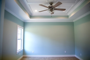 White tray master bedroom ceiling in small new construction house with windows and a ceiling fan and pale blue turquoise walls