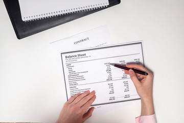 Balance sheet and other documents are checked by female hands with pen. Accounting concept