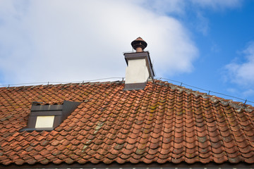 Fragment of old weathered ceramic red tile roof on the background of blue sky.