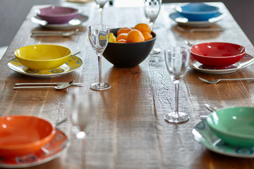 Wooden table with empty coloured dinnerware, prepared for lunch or dinner. Modern interior. Small depth of field.