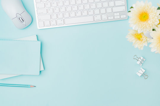 Flat lay blogger or freelancer workspace with a keyboard, flowers in a vase, office supplies on a color background