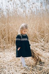 little girl with blond hair in a black luxurious dress on a background of a golden field