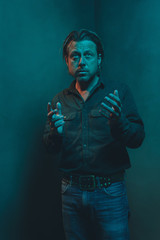 Man in green shirt and jeans stands in corner of empty room. Making gesture with hands.