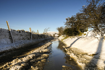Winter scene of a snow covered wall and fence with water on a mountain road