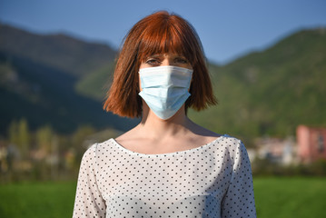 Girl in protective mask with flowers on the background of nature. Post-apocalypse survival after the covid-19 coronavirus pandemic. World after global catastrophe - obrazy, fototapety, plakaty