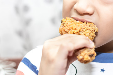 Hungry little boy eating chicken leg. Child hand holding a fried chicken.