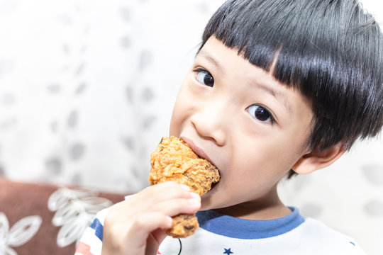 Hungry asia little boy eating chicken leg. Child hand holding a fried chicken.