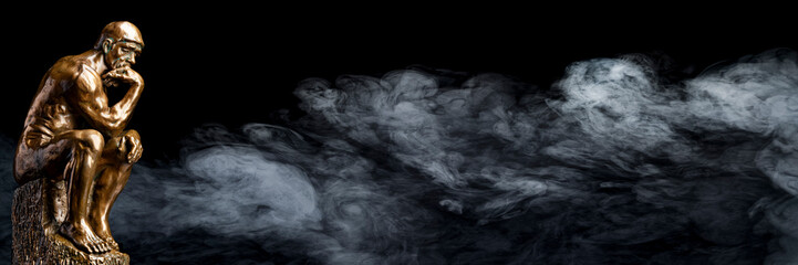 A bronze replica statue of Rodin's Thinker on a smoky background