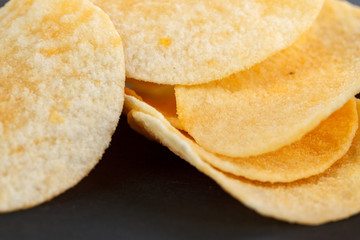 Classic potato chips. Fast food snack isolated on black background. A pile of crispy chips close-up as a background. Unhealthy food.
