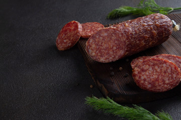 Dark banner of smoked sausage. Sausage cut from meat on a wooden Board with herbs and black pepper. Gloomy mood. Creative and delicious serving. Low key. Copy space