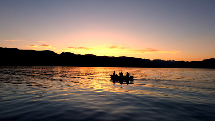 4 people fishing in a boat floating on Hebgen Lake during colorful sunset.
