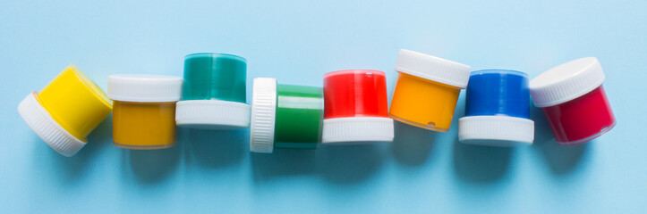 Plastic jars with multicolored gouache paints close up on a blue background and copy space