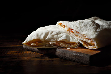 Shawarma on a black background. Salad wrapped in pita bread on a dark board.