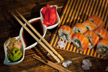 Sushi on a bamboo plate. Sushi roll with sauce and spices on a black background. Food on a wooden table with dark boards. Sakura color on a plate. Flower with rose petals.