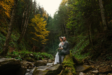 the bride and groom are sitting on a stone in the middle of a mountain river in the forest. Mountain wedding. Wedding in the forest.