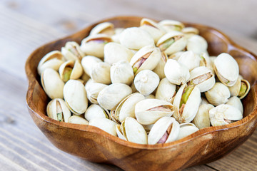 Heap of ripe pistachios in the wooden bowl closeup. Healthy mediterranean fruit, full of vitamins and minerals. Vegetarian diet food.