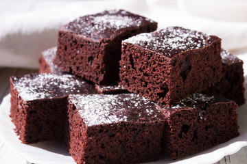 Chocolate cake cut into square pieces, sprinkled with icing sugar on a plate, white background