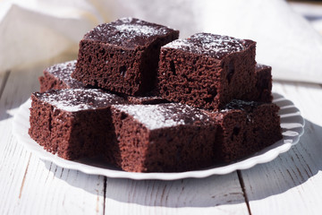 Chocolate cake cut into square pieces, sprinkled with icing sugar on a plate, white background