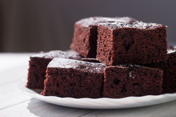 Chocolate cake cut into square pieces, sprinkled with icing sugar on a plate, white background