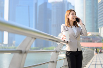 Fototapeta premium Business person, Coffee break and using phone concept, Young Asian woman holding portable-coffee mug and using smart phone while coffee break in urban city