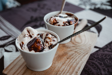Containers with vanilla ice cream and liquid chocolate ready to eat on a wooden board