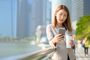 Business person, Coffee break and using phone concept, Young Asian woman holding portable-coffee mug and using smart phone while coffee break in urban city