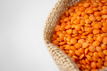 Red lentils in rustic cloth bag isolated on white background