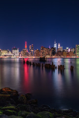 Obraz premium Midtown Manhattan at night from East river ,Empire state building is in red lights