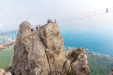 People crossing chasm on rope bridge in mountains on blue sea and sky background