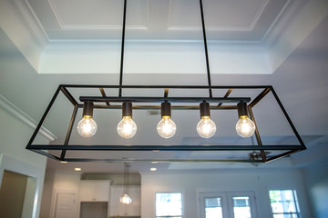 Hanging retro black metal iron chandelier lighting fixture with vintage bulbs hanging in a dining room of a new construction house