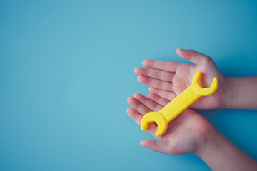 Kid girl hands holding yellow wrench toy on blue background.Concept for brain fix, child development, Broken family, Renovate home, Recovery mind, Engineer education, Learn creative kid, Workshop.