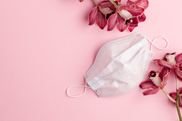 Protection with tenderness. Medical concept. Surgical mask on a pink background with delicate pink orchids. Copy space