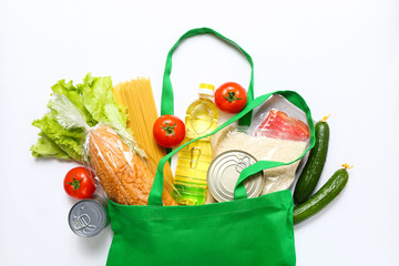 Set of grocery items from vegetables, canned food, pasta, oil, cereal in green eco shopping bag on white background. Top view.