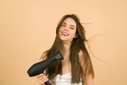 Hair dryer. Portrait of attractive girl with brunette hair using hairdryer. Hairstyle, hairdressing concept. Girl using hair dryer in the Morning, on a beige background.