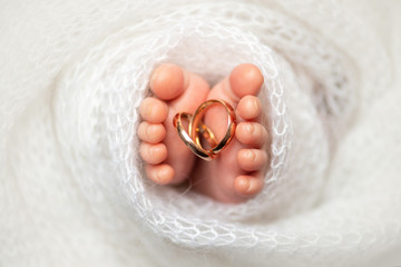 Closeup newborn baby feet with wedding rings in the white blanket. The concept of the family. 