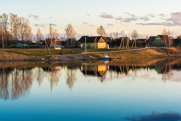 Obraz premium urban village or village with wooden houses located on the blue river bank, early spring evening at sunset