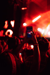 People taking photographs with smart phone during a music festival. Fans enjoying rock concert with light show and clapping hands.