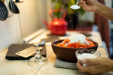 expolvorear azucar sobre tomates cortados en un cuenco de madera
en la cocina de un hogar