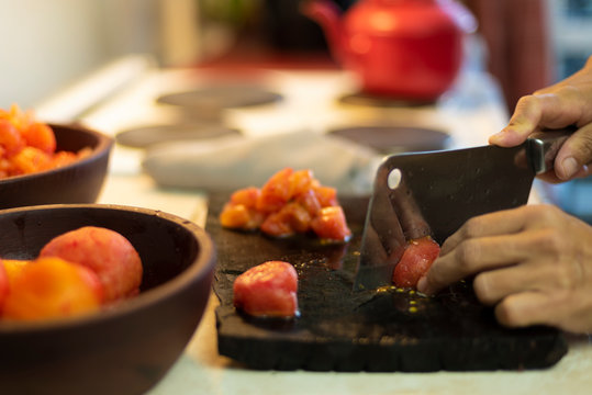 manos cortando tomates con una cuchilla sobre tabla de madera en la cocina de un hogar