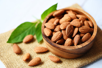 Almonds nuts on wooden bowl with leaf almonds top view on sack background - Roasted almond for snack