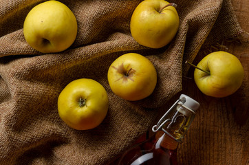 Full bottle of cider with basket of yellow apples.