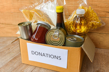 Donations box with canned food on wooden table background / pasta canned goods and dry food non...