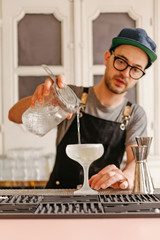 Vertical photo of a waiter transferring liquid into a glass with ice to a frost cocktail glass