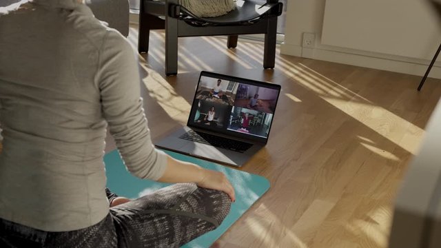 Fitness trainer conducting virtual yoga class with group of people at home on a video conference. Fitness instructor taking online yoga classes over a video call on laptop.
