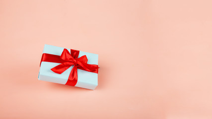 Gift wrap in blue with a red and pink ribbon on a pink backing. Levitation. Lifting into the air. Copy space. Concept of sales, discounts, holiday gifts and purchases.