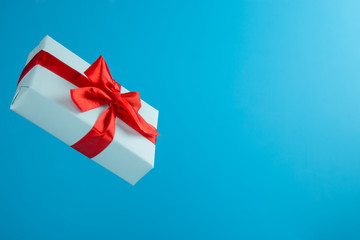 Gift package blue with red pink ribbon on blue trending color. Levitation. Raising in air. Сopyspace. Concept of sale, discounts, holiday gifts and purchases.