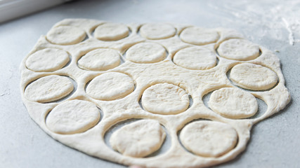 Preparation of the dough for baking, freezing, sculpting and other food blanks - a large piece of the dough is on the table and the chef cuts out small circles on it with an iron shape. Moulding