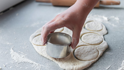 Preparation of the dough for baking, freezing, sculpting and other food blanks - a large piece of the dough is on the table and the chef cuts out small circles on it with an iron shape. Moulding