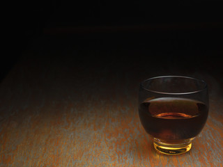 A small glass of scotch whiskey or bourbon on the wooden countertop. A shot of spirits.